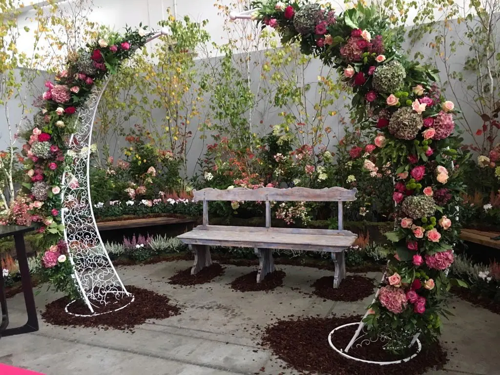Arco floreale con rose rosa e panca, allestimento da esposizione