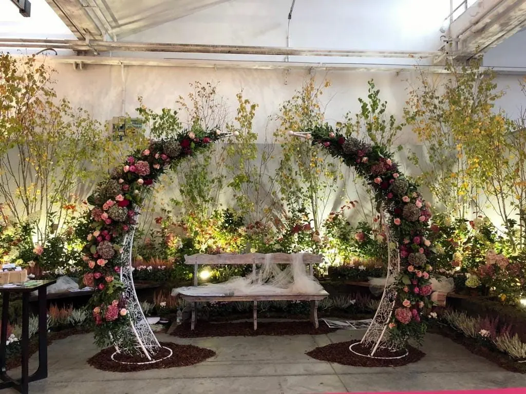 Arco fiorito con rose e rami, allestito in uno spazio espositivo
