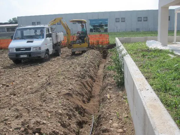 Autocarro e miniescavatore al lavoro su una trincea lungo un muretto nuovo