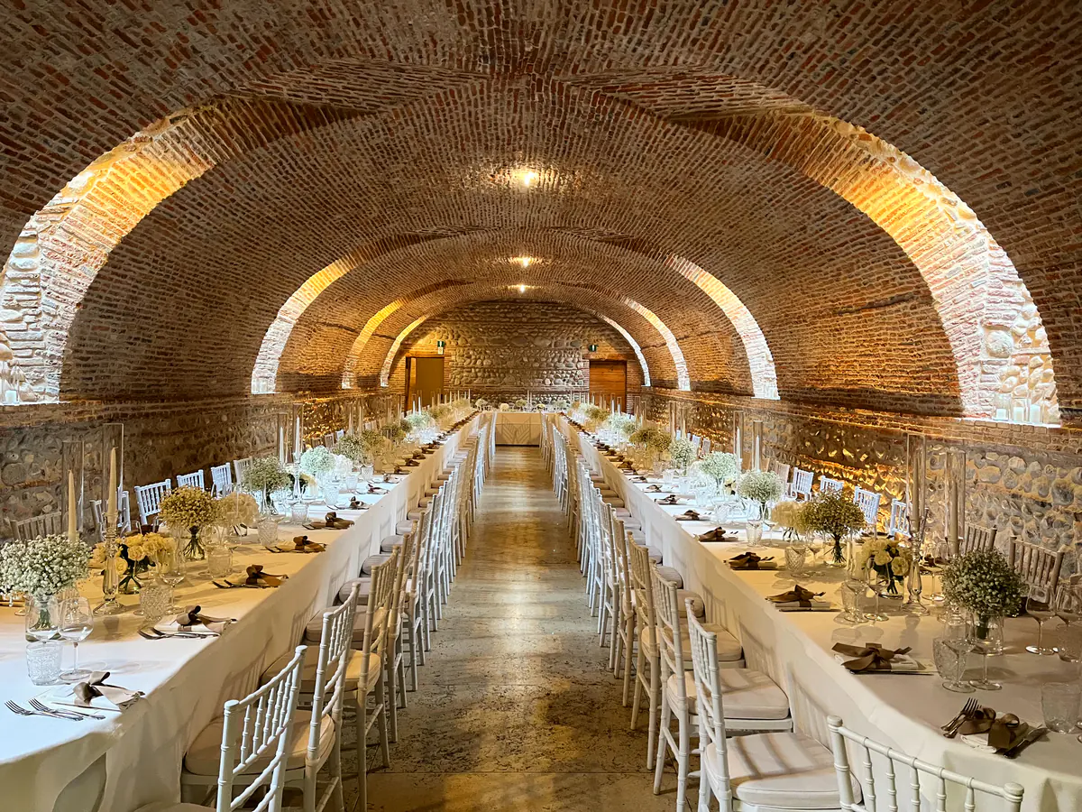 Cantina a volta in mattoni con lunghe tavolate apparecchiate e fiori